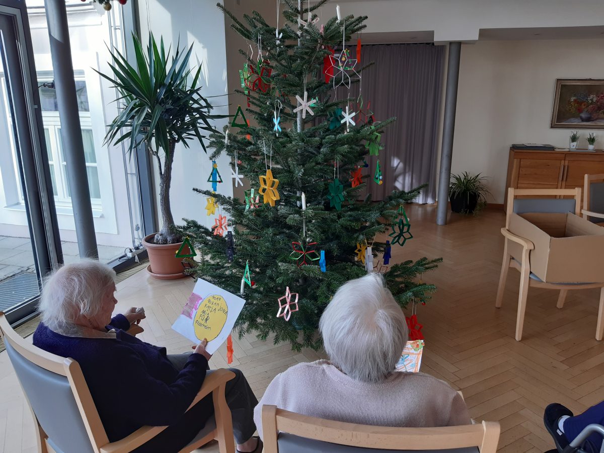 Zwei Seniorinnen sitzen mit Bastelarbeiten vor einem geschmückten Weihnachtsbaum.