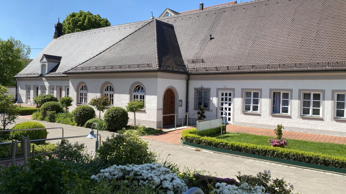 Seitenansicht auf den Kapellenbau, eingefasst von Rosen- und Buchsbäumchen.